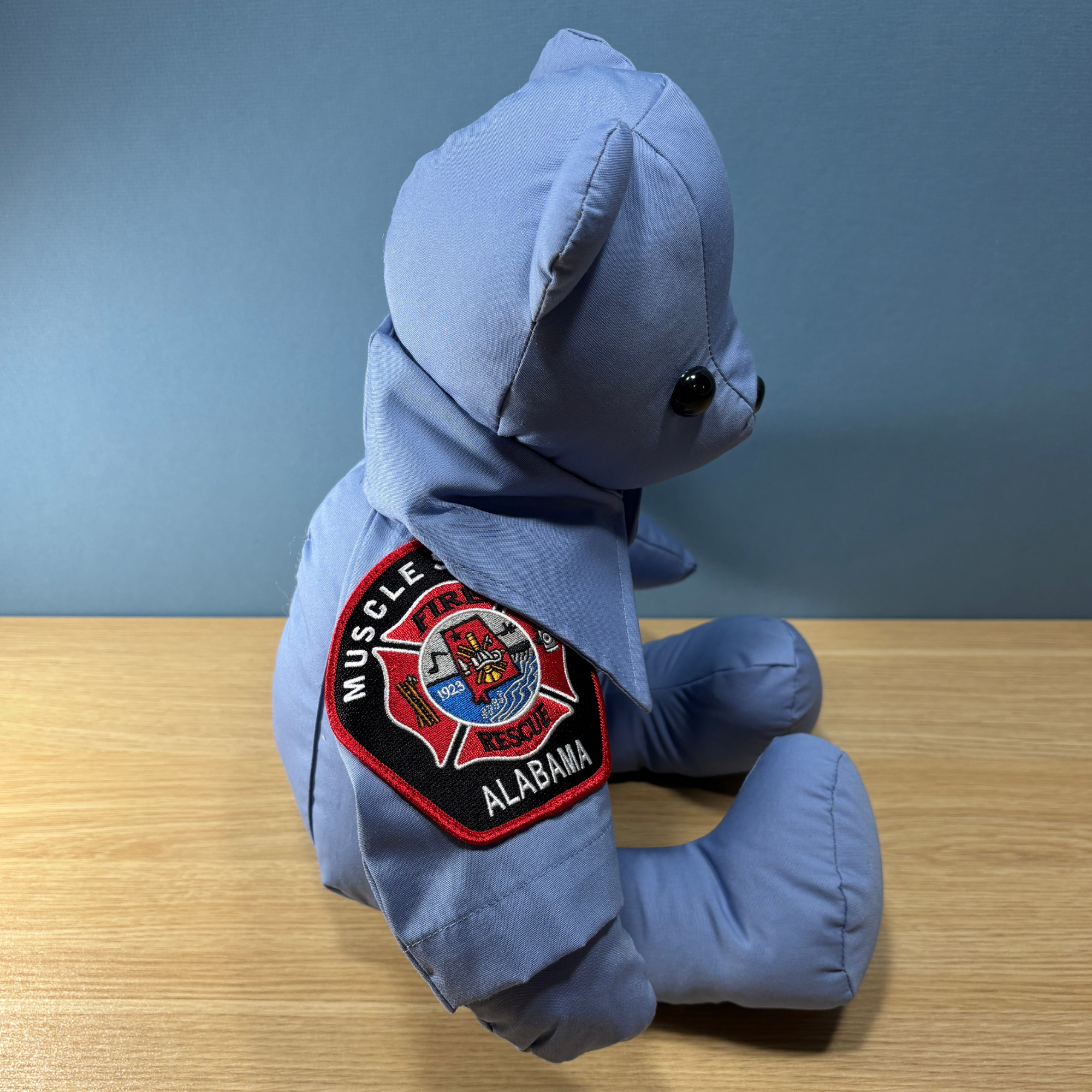 side view of the firefighter memory bear showing the fire department patch on the sleeve of the shirt 